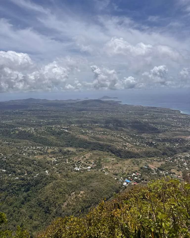 The interior and coastline of Saint Lucia from high on a ridge, settlements scattered across forested hills with the sea and a small island on the horizon